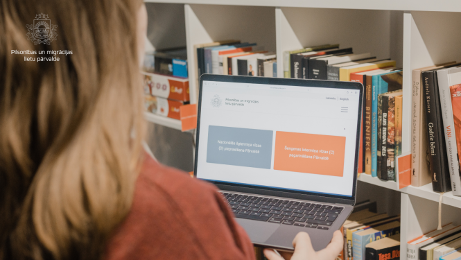 Persona pie grāmatu plaukta skatās portatīvajā datorā, kur atvērta Pilsonības un migrācijas lietu pārvaldes mājaslapa ar vīzas pieteikšanas pogām.