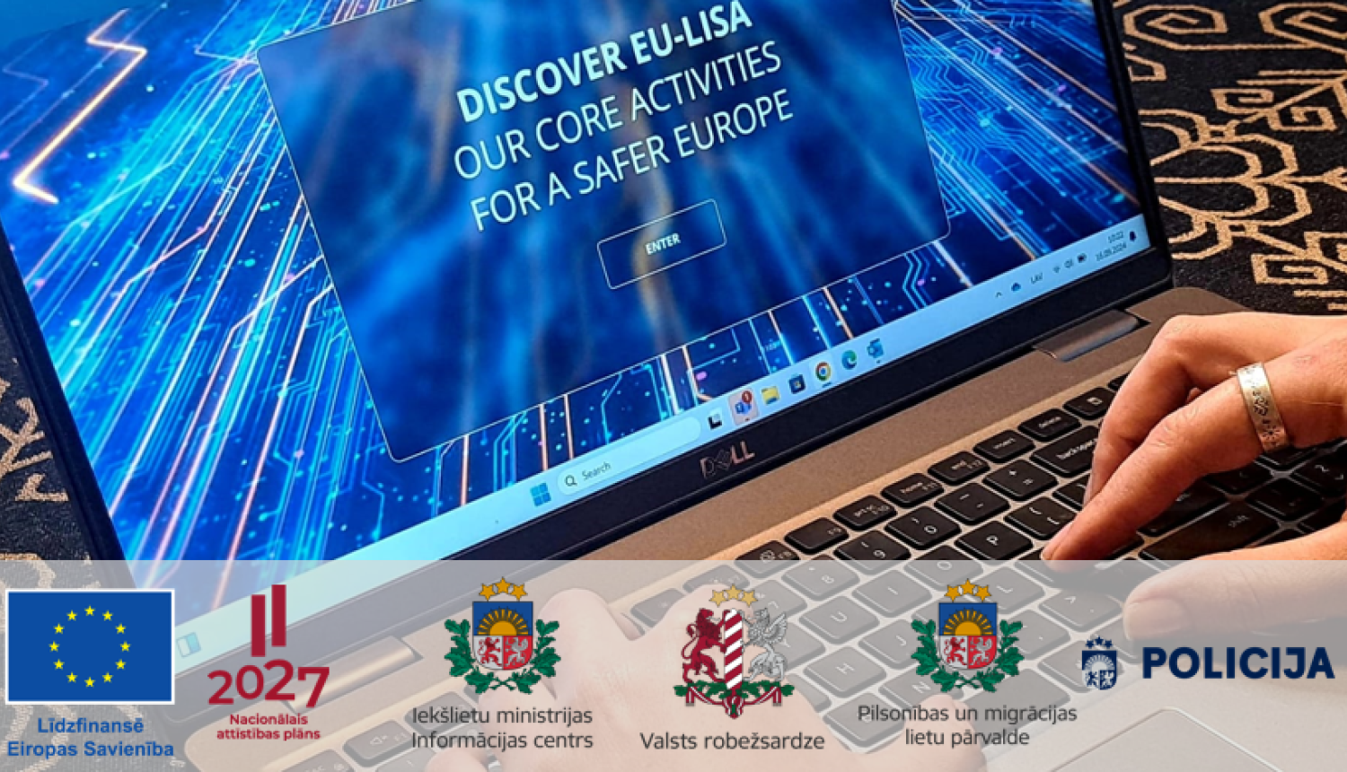 Portatīvā datora fotoattēls ar ekrānā redzamu datu pārraides māksliniecisku shēmu un uzrakstu angļu valodā "Discover EU-Lisa, our core activities for a safer Europe", kā arī Eiropas Savienības līdzfinansējuma, Latvijas Nacionālā attīstības plāna, Iekšlietu ministrijas Informācijas centra, Valsts robežsardzes, Pilsonības un migrācijas lietu pārvaldes un Valsts policijas logotipi.