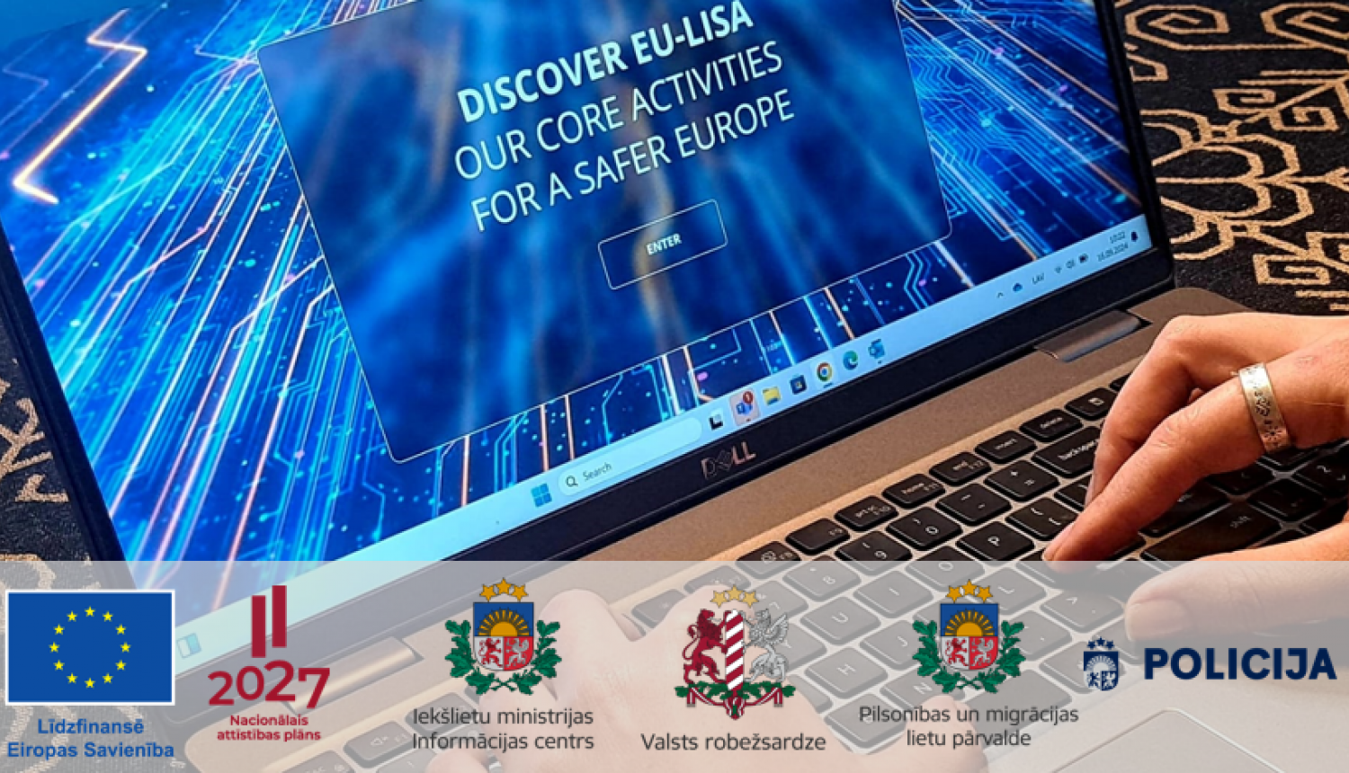 Portatīvā datora fotoattēls ar ekrānā redzamu datu pārraides māksliniecisku shēmu un uzrakstu angļu valodā "Discover EU-Lisa, our core activities for a safer Europe", kā arī Eiropas Savienības līdzfinansējuma, Latvijas Nacionālā attīstības plāna, Iekšlietu ministrijas Informācijas centra, Valsts robežsardzes, Pilsonības un migrācijas lietu pārvaldes un Valsts policijas logotipi.